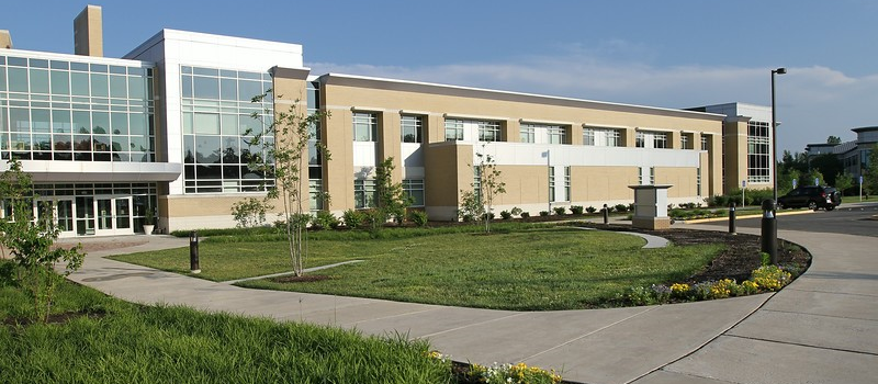 The image depicts a UMW building at sunrise on a beautiful clear blue sky day.