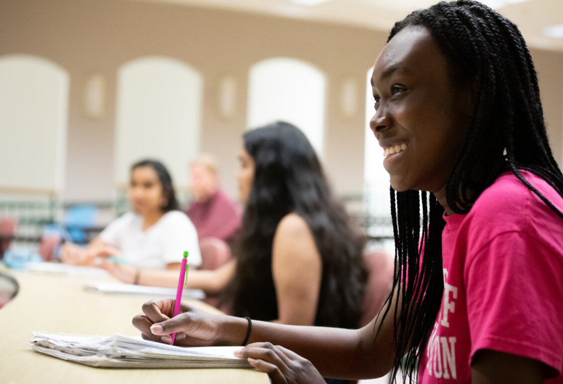 A student smiling as she takes notes.