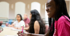A student smiling as she takes notes.