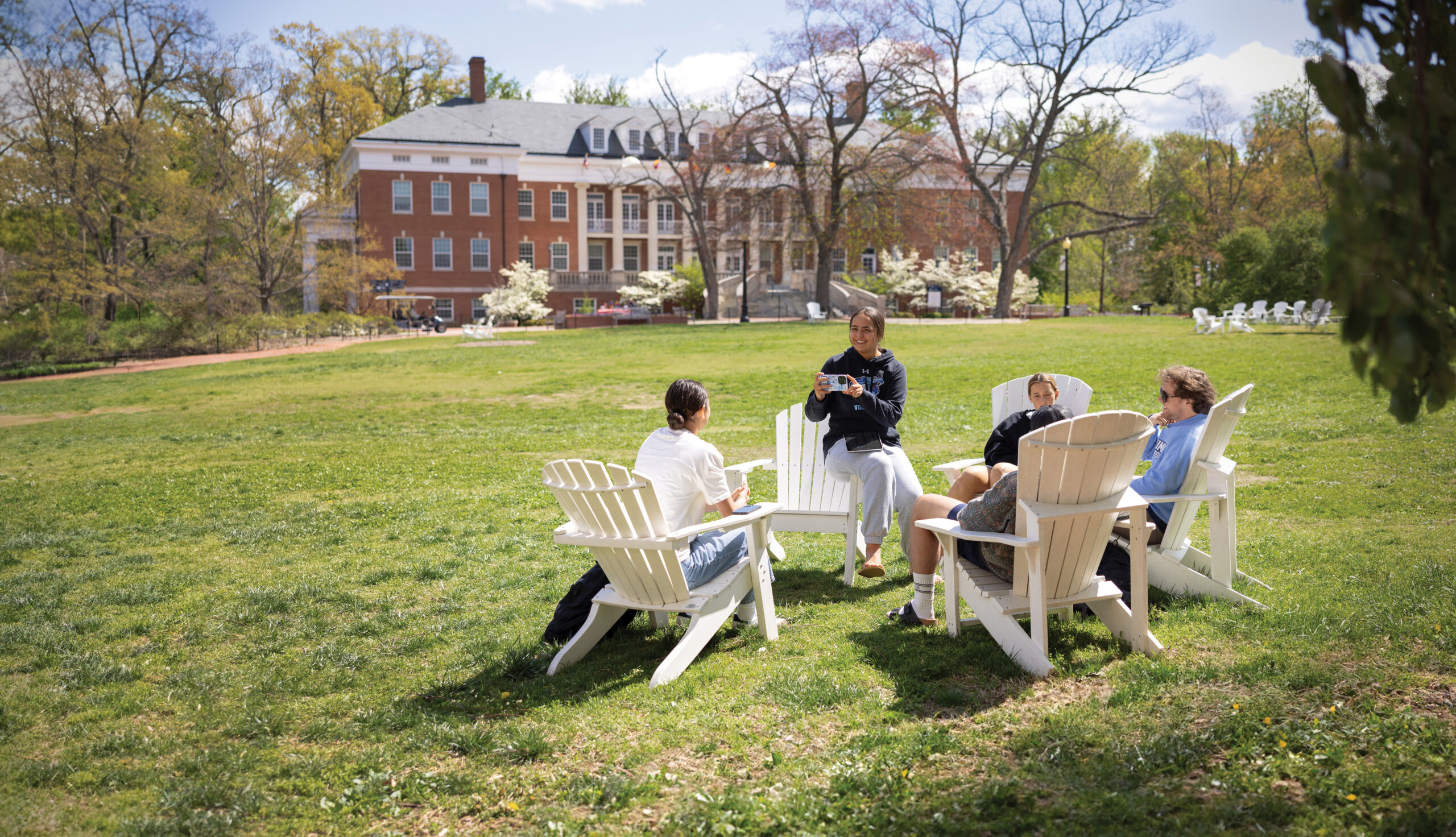 Four students sitting in Adirondack chairs in the center of campus