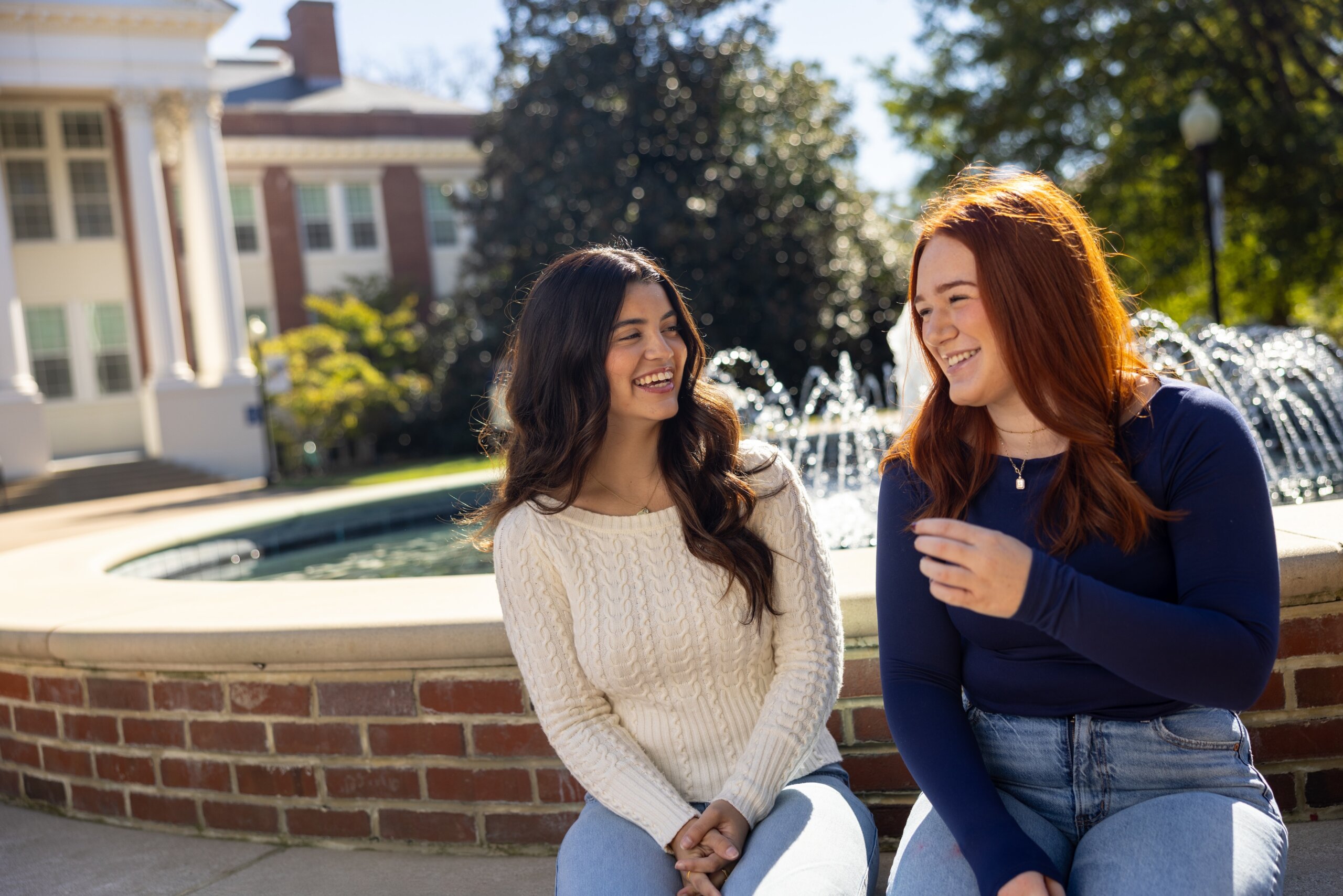Two women laughing in front of the fountain on campus