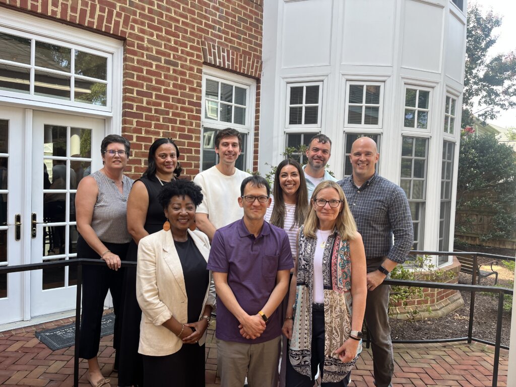 Nine faculty fellows and industry fellows standing outside a brick building