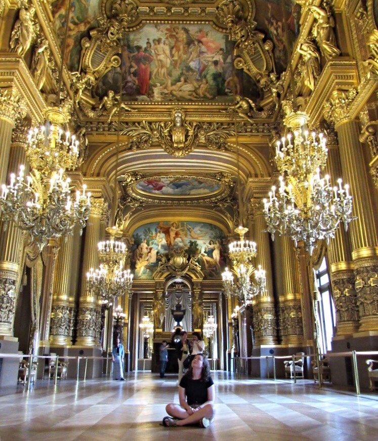 Student sitting on the floor in a large, lavish chamber looking at artwork on the ceiling.
