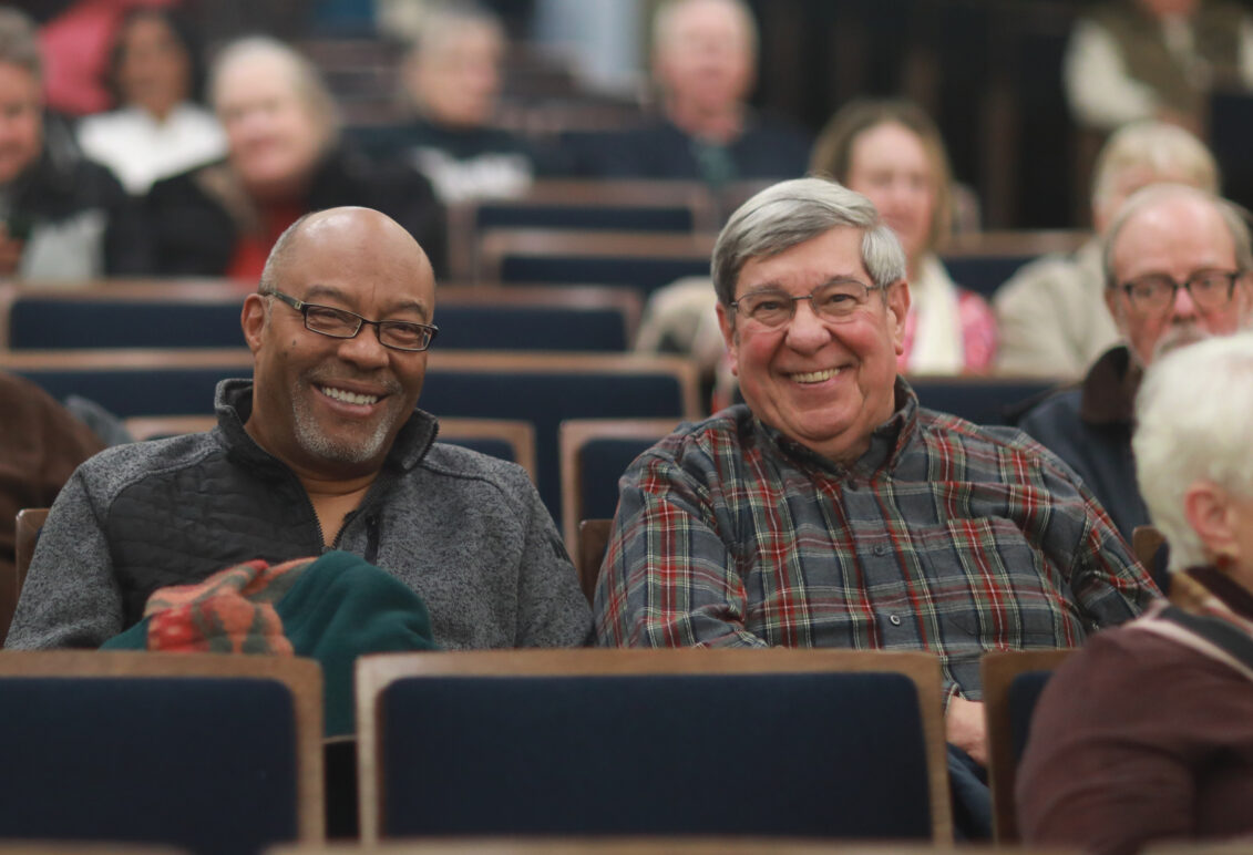 Two men sitting in the audience in Dodd Auditorium smiling at the camera.