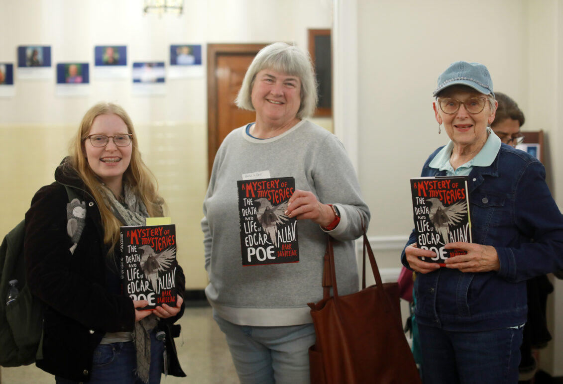 Three attendees holding the book titled, "A Mystery of Mysteries: The Death and Life of Edgar Allan Poe" by Mark Dawidziak.