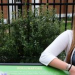 Senior biology and environmental sciences major Maggie Magliato poses with a sign from the pollinator walk she created on campus. Photo by Norm Shafer.