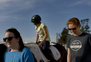 UMW sophomores Hannah Backe (far left) and Elizabeth Finto (far left) volunteer on a recent Tuesday night with the therapeutic horseback riding program at Hazelwild Farm. Photo by Reza A. Marvashti.