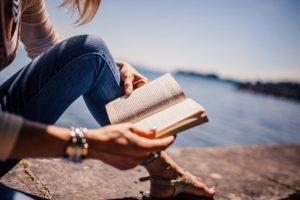 person sitting near water reading book