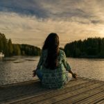 person sitting in yoga pose at end of dock overlooking water