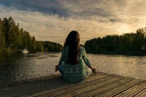 person sitting in yoga pose at end of dock overlooking water