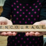 person holding scrabble letters to spell 'encourage'.