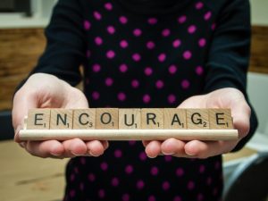 person holding scrabble letters to spell 'encourage'. 