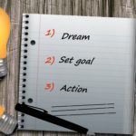 notepad surrounded by lightbulbs. notepad reads a list; dream, set goal, action.