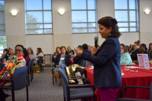 woman holding microphone reading from note card speaking to audience