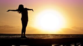 sun in background and person standing with arms open.