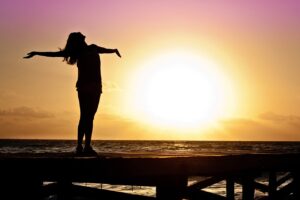 sun in background and person standing with arms open.