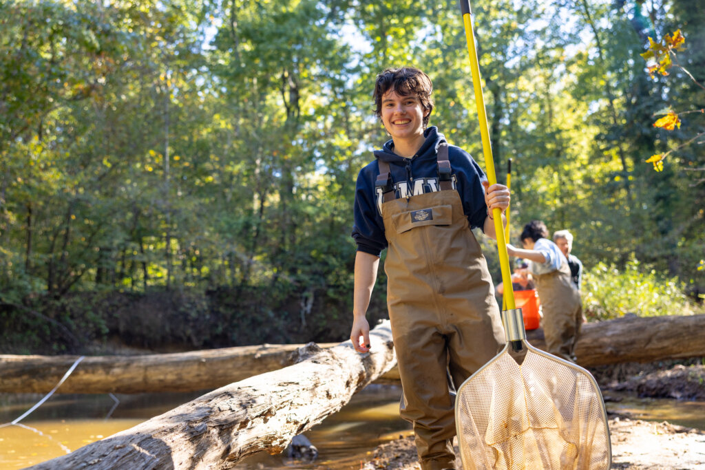 Student holding fish net in a creek. 