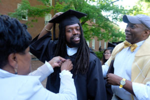 Mario Catlett gets help with his regalia from his mother Marci Catlett and Dean Rucker.