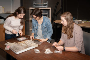 From left to right, Reagan Anderson '17, Olivia Larson '19 and Alison Cramer '17 examine artifacts at Dovetail.