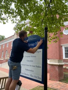 Facilities Services' Micy Wallace changes the sign outside Trinkle Hall, renamed today as James Farmer Hall. With the vote by UMW's BOV to rename the building, a beloved member of the Mary Washington community who spent most of his career fighting injustices, is memorialized.