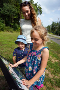 Walking along the Rappahannock Heritage Trail, Stephanie Gardner and her kids, Piper and Pierce, read 'Alex's Day on the Rappahannock,' written and illustrated by students in UMW's College of Education, as part of Fredericksburg Parks, Recreation and Events department's new StoryWalk(R) project. Photo by Suzanne Carr Rossi.