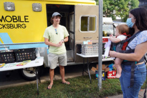 Hollis Cobb stands next to the Fredericksburg Bookmobile and chats with local residents browsing for books at the Fredericksburg farmer's market. Photo by Suzanne Carr Rossi.