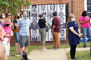 Onlookers gaze at the banner featuring the mug shots of the original Freedom Riders, including the late Dr. James Farmer (first photo in second row) and the late Rep. John Lewis (fourth photo in third row). Photo by Suzanne Carr Rossi.