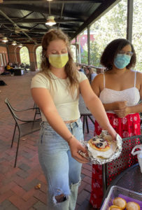 Hannah Iezzi shows off a mini pizza made as Mandy Byrd looks on. Every Monday, the class gathers on the Eagle's Nest patio to enjoy homemade dishes using items the students find at the Co-op that have met their "best by" date. Photo by Maggie Ellis.