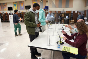 Mary Washington senior Darius Reed (front, left), who studies sociology and Spanish, and runs track, talks with UMW Digital Knowledge Center Shannon Hauser, who was working the polls, in preparation for casting his ballot at Walker-Grant Middle School in Fredericksburg. Photo by Suzanne Carr Rossi.