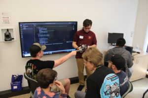 From left, King George high school students Sonny Martin, Keegan Kearl and Christopher Ashley, work alongside team mentor MITRE Software Engineer Ariel Burdette, and teammates Sean Bless and Rodrigo Alexander Veliz during the first annual Innovation Challenge @ Dahlgren. Photo by Paige Shiplett.