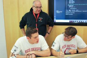 Ethan Kane (left) and Jameson Scott work in the foreground on coding, while their team leader, retired Air Force Master Sgt. Doug French, who heads the JROTC program at Lancaster High School. Photo by Paige Shiplett.