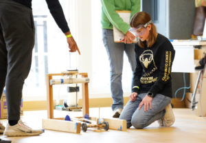 Lily Jacoby thinks through her entry in the 'Scrambler' event. That contest had teams testing the mechanical devices they designed to use energy from a falling mass to transport an egg along a straight track and stop as close to the center of a barrier as possible without breaking the egg. Photo by Suzanne Carr Rossi.