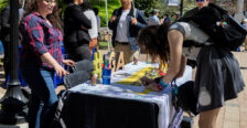 A student bends over a table to write something while other students surround the table, which is topped with an "#SGA" decoration