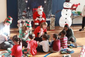 From left to right, UMW COAR members Knox McKinley, Ainsley Lord and Khushi Constance (along with Center for Community Engagement Director Sarah Dewees, in red) talk to children as they open their gifts. Photo by Karen Pearlman.