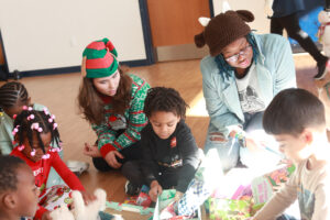 UMW sophomore Ainsley Lord (left) and alumna Tamara Garrett '23 talk with preschool children from Fredericksburg City Public Schools as they open gift boxes delivered by COAR. Photo by Karen Pearlman.