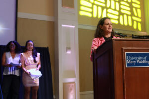 Juliette Landphair speaks of the extraordinary excitement she's seen on campus this year, while co-hosts and UMW seniors Martina Nicholson (far left) and Kai Ortero (middle) listen on, during the annual Eagle Awards presentation. Photo by Karen Pearlman.