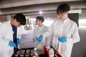 From left: High schoolers Michael Young, Alexander Rosas and Vincent Phan dip cotton balls in washable paints before lobbing them at black canvases to create artwork resembling evolving stellar clusters, which they learned about in an astrophysics lesson. Photo by K Pearlman Photography.