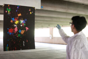 Alexander Rosas, a senior at Stafford High School, shows off his strategy of using heavily painted cotton balls on the right side of the canvas and reused cotton balls on the left side to demonstrate that the amount of energy put into an object correlates to its outcome. Rosas, who is involved with robotics and technology clubs in high school, said he was excited to connect with members of the physics community in Fredericksburg by participating in the PING program. Photo by K Pearlman Photography.