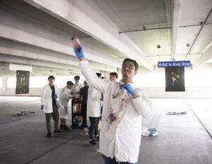 High schooler Maiwand Barakzai chucks a painted cotton ball at a canvas while his classmates look on. Photo by K Pearlman Photography.