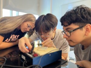 Hannah Steele ’26, a UMW student mentor and Noyce Scholarship recipient, guides high schoolers Vincent Phan (left) and Alexander Rosas in creating a circuit. Photo by Katie Van Houten ’27.