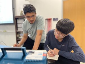 High schoolers Maiwand Barakzai (left) and Michael Young make notes as they learn about creating circuits. Photo by Katie Van Houten ’27.