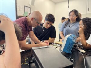 UMW Physics Chair and Professor Matt Fleenor demonstrates how to construct a circuit to high schooler Zubair Mohammadzai (center), while UMW student mentor Aliya Ather and volunteer mentor Emma Wallach (right) observe. Photo by Katie Van Houten '27.