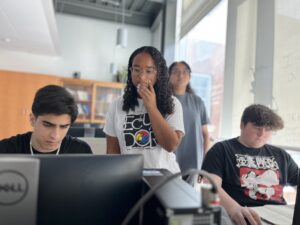 High schoolers Zubair Mohammadzai (left) and Tristan Towle (right) are guided in a lesson by volunteer mentor Emma Wallach, a Stafford High School junior who already participated in the PING program at Michigan State University, and UMW mentor Aliya Ather ’28 (background). Photo by Katie Van Houten ’27.