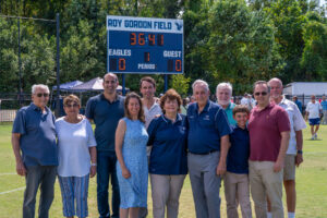 Coach Gordon poses with wife Terrie and their family in front of the scoreboard that overlooks the Roy Gordon Field. Photo by Kaitlynn Kimball.