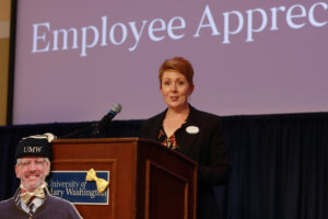 Executive Director of Human Resources Beth Williams addresses the crowd at the Employee Appreciation Luncheon behind a cutout of President Paino, who was unable to attend the event. Photo by Karen Pearlman.