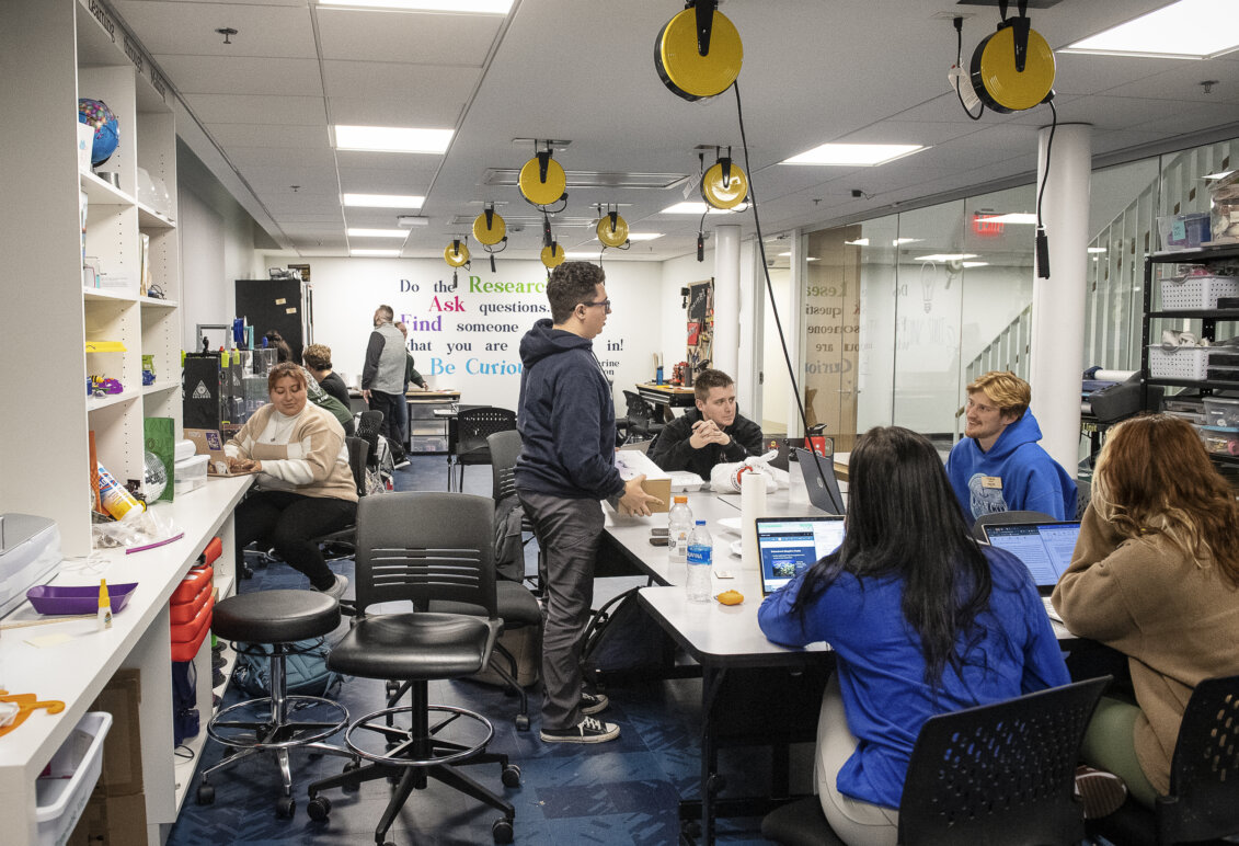Several students are gathered in a creative space with gadgets and innovative objects galore
