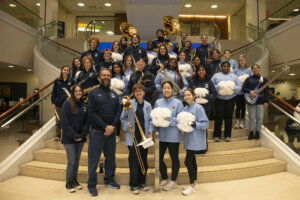 The UMW Pep Band and Pep Dance, with instruments and pom-poms in hand, stand on the steps in the Cedric Rucker University Center.