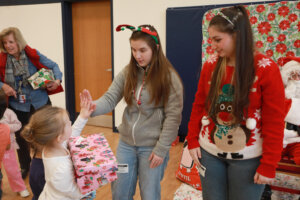 A University of Mary Washington student gives a high-five to a smiling preschool child holding a gift box