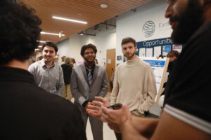 Students stand in a hallway listening to a scientific research presentation beside a poster on microglial inflammation and Alzheimer’s disease.