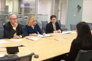 A panel of three judges question a college student, who is seated across the table.